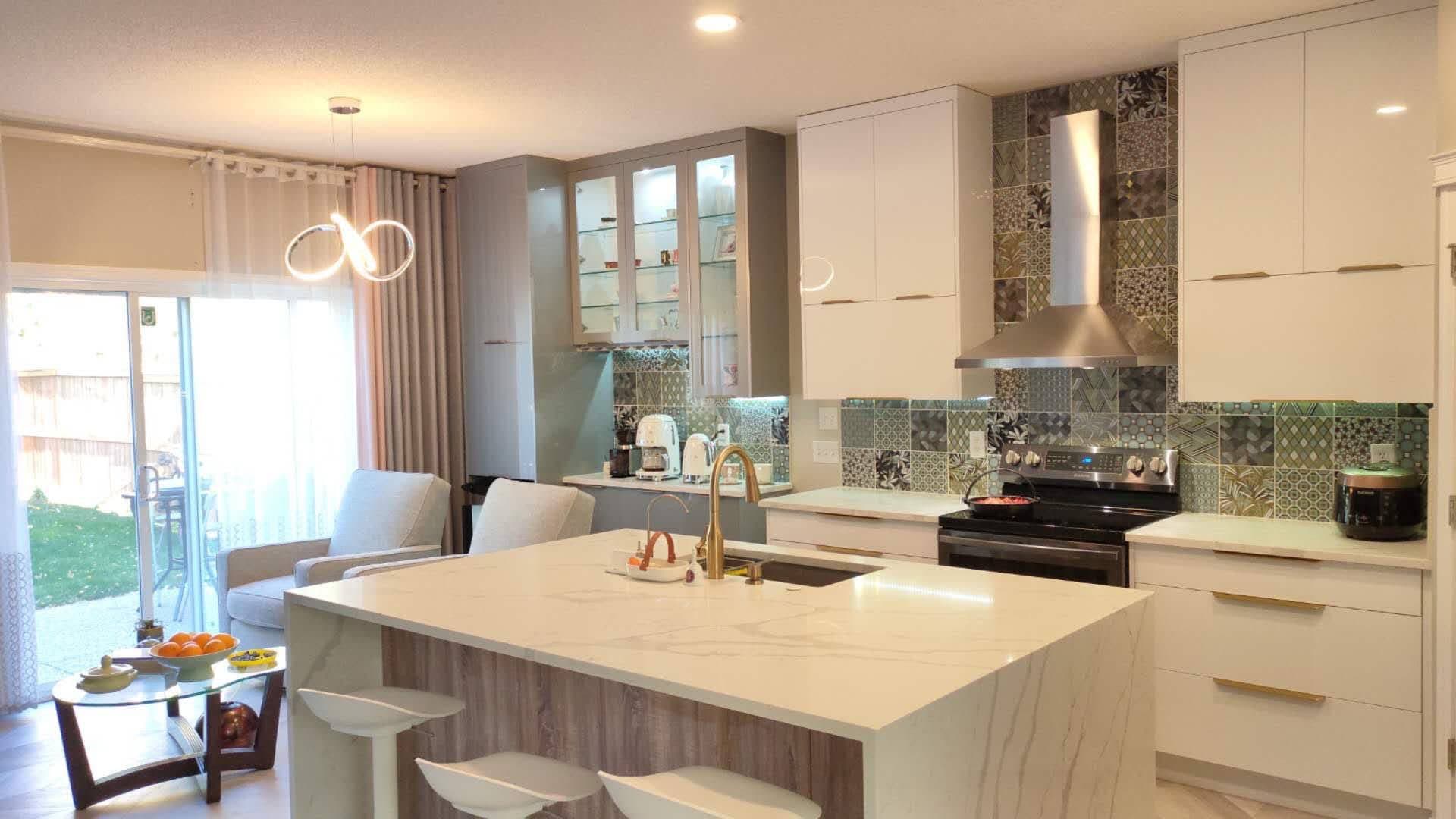 Modern kitchen with white and grey Calgary custom cabinets, large quartz island, patterned tile backsplash, gold accents, and an open concept living area.