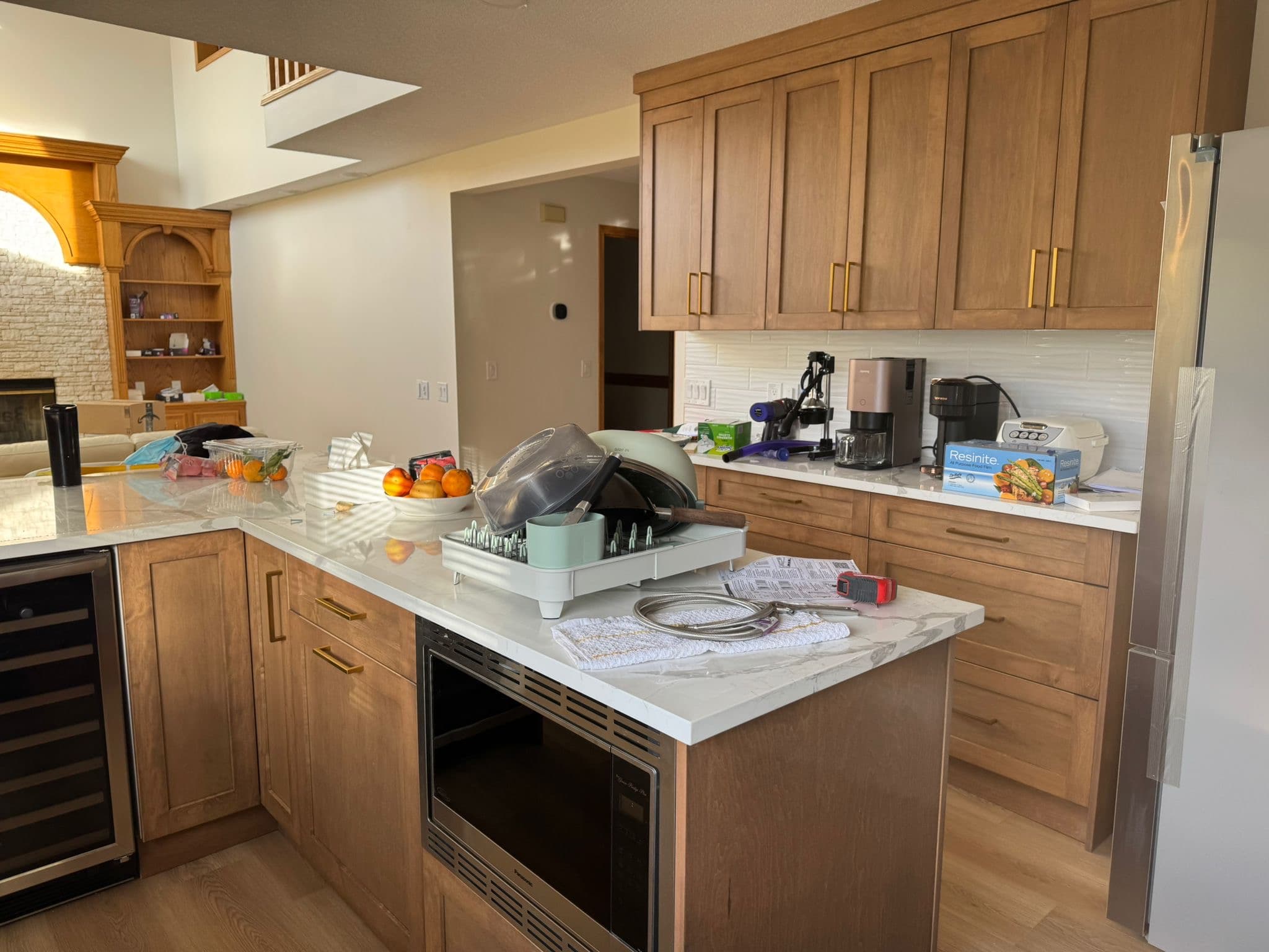 A spacious kitchen features warm-toned wooden Calgary custom cabinets with brass hardware, a large island with a microwave, and a wine cooler, creating a functional and inviting space.